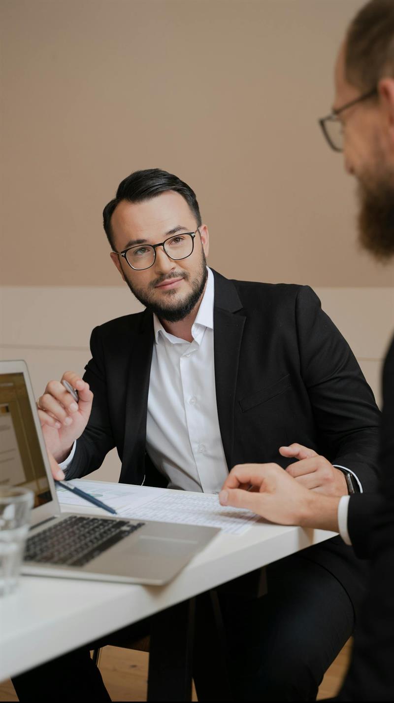 Zwei Männer an Bürotisch, auf dem ein Laptop liegt