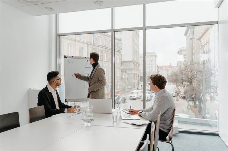 Ein Mann am Flipchart stehend und zwei Männer an Tisch sitzend in Konferenzraum