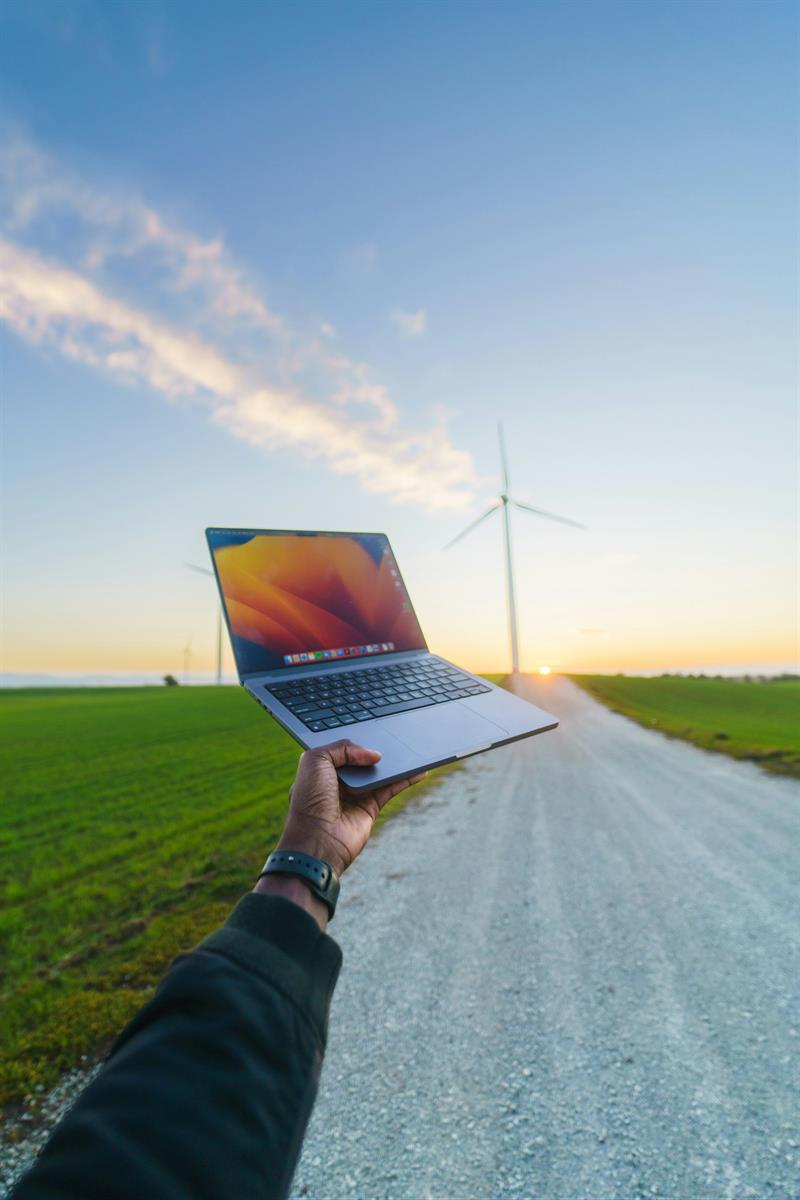 Eine Hand hält einen Laptop in die Luft und im Hintergrund steht ein Windrad