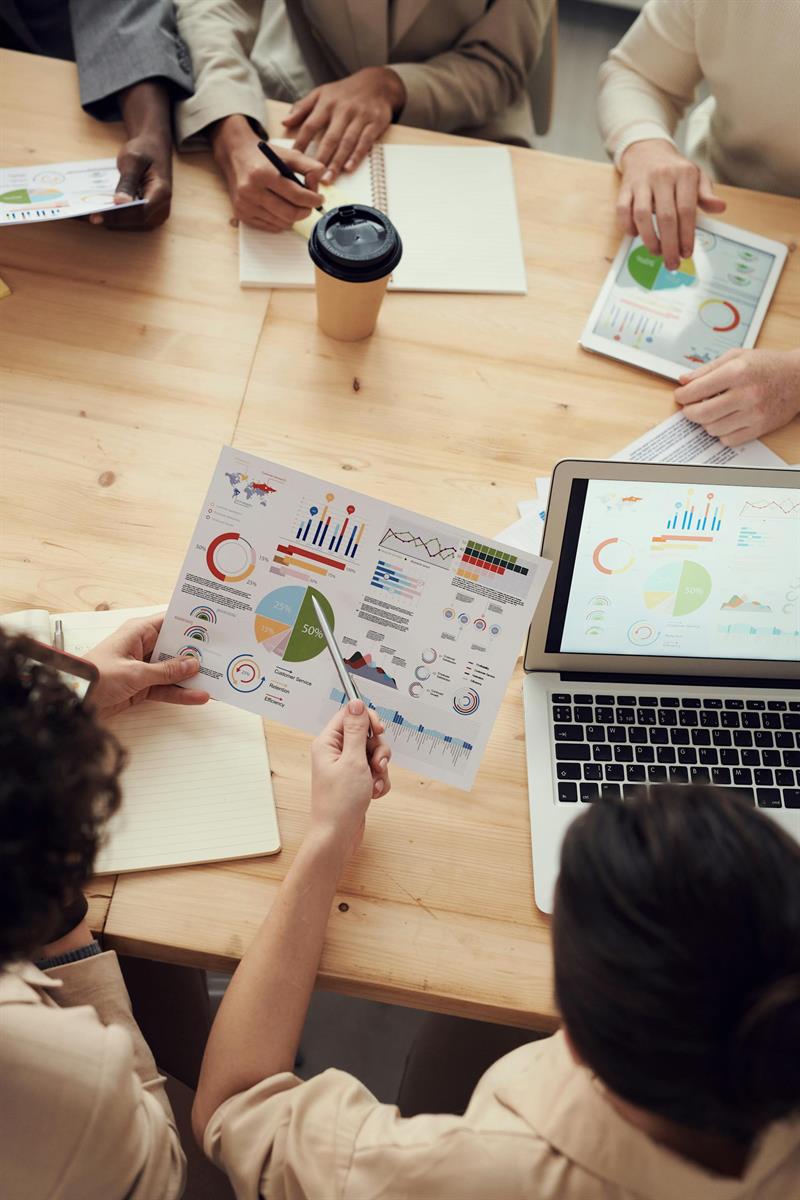Fünf Personen um einen Holztisch mit Laptop, Tablet und Papier mit Diagrammen